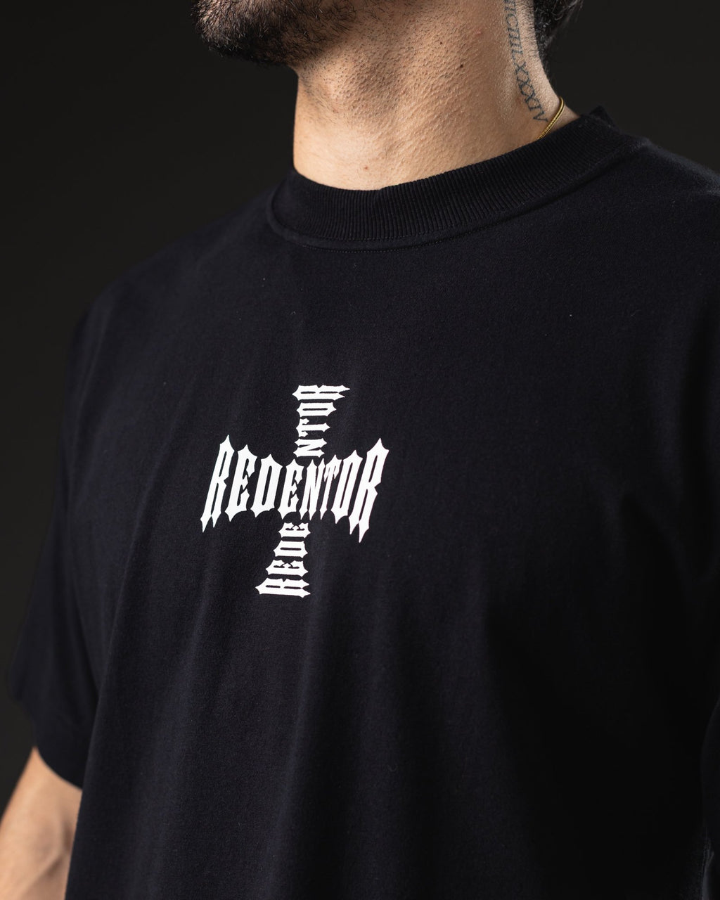 Detalle del logo Redentor en forma de cruz estampado en blanco sobre el pecho